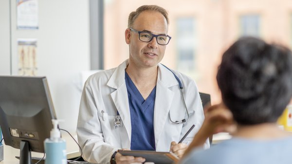 Ein Arzt sitzt am Schreibtisch und spricht mit einer Patientin.