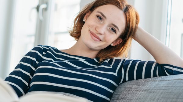 Eine Frau auf einem Sofa schaut lächelnd in die Kamera.