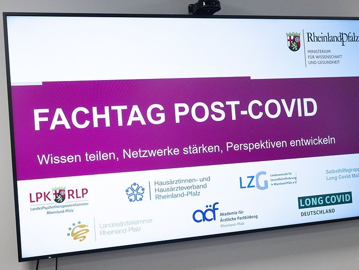 Ein Monitor, auf dem ein Hinweis auf den Fachtag Post-Covid hingewiesen wird