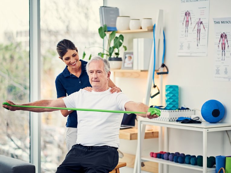 Ein Mann macht Kraftübungen, begleitet von einer Physiotherapeutin.