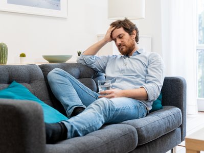 Ein Mann mit Kopfschmerzen ruht sich auf einem Sofa aus.